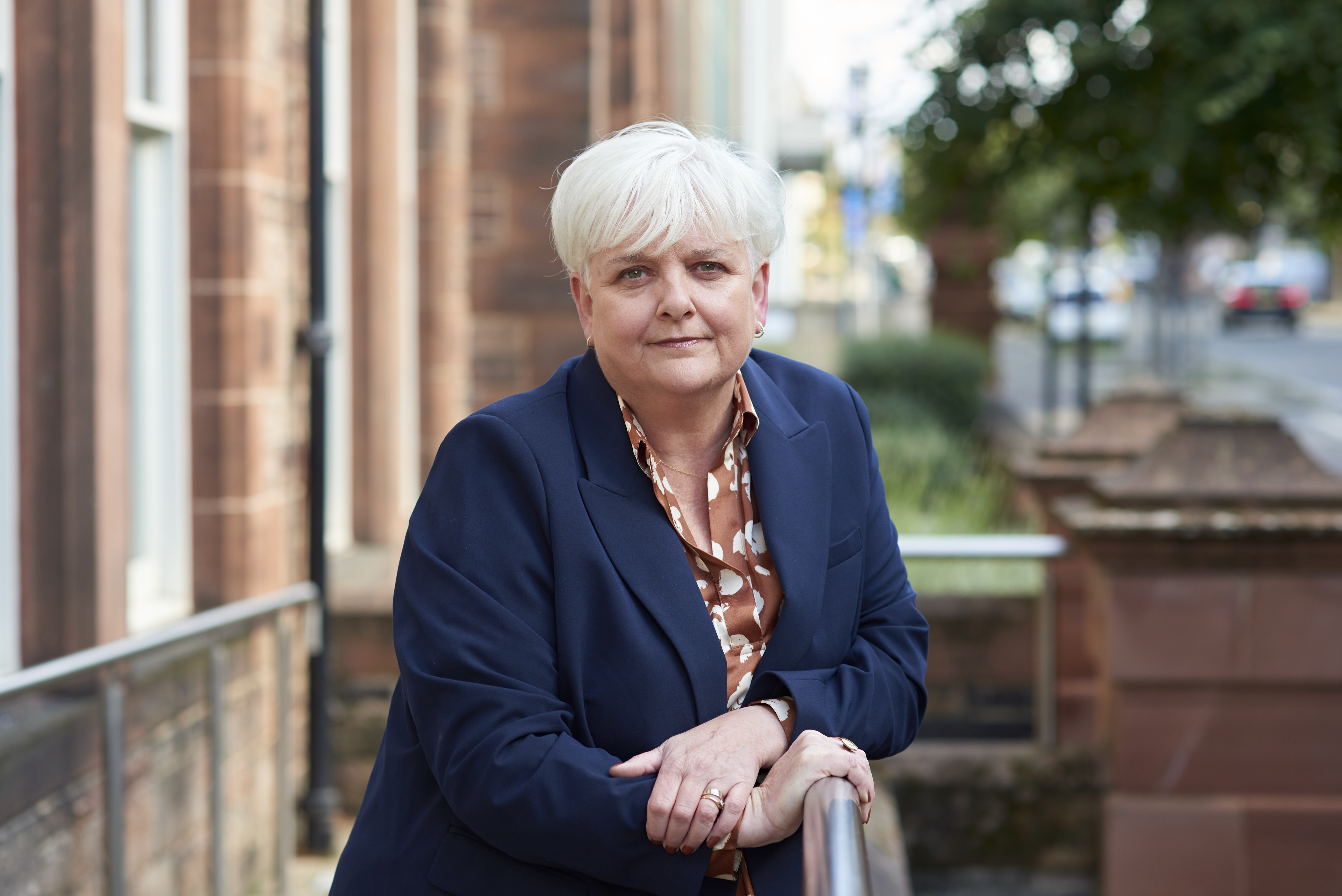 Professor Angela O'Hagan frowning and leaning on a railing outside of the SHRC office