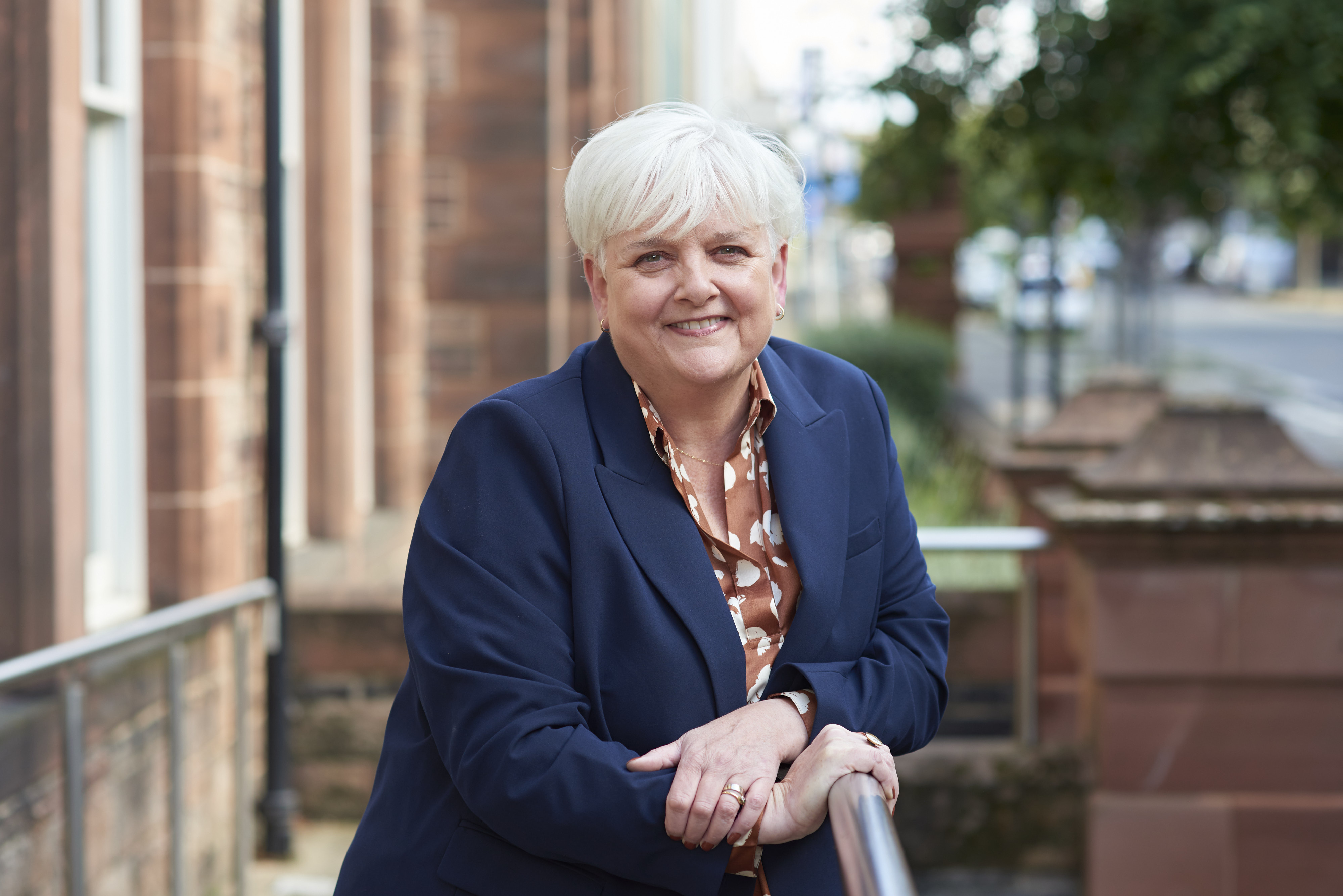 Professor Angela O'Hagan smiling and leaning on a railing outside of the SHRC office