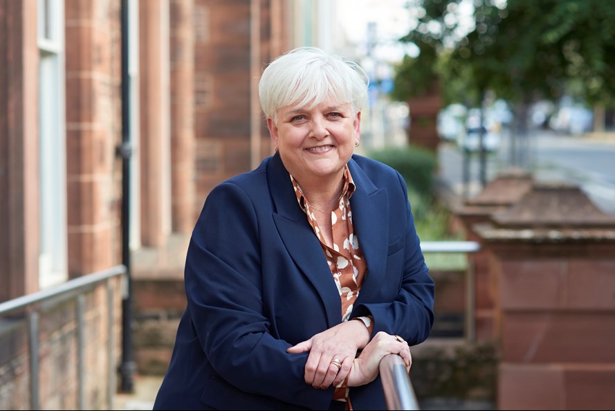 Professor Angela O'Hagan smiling and leaning on a railing outside of the SHRC office